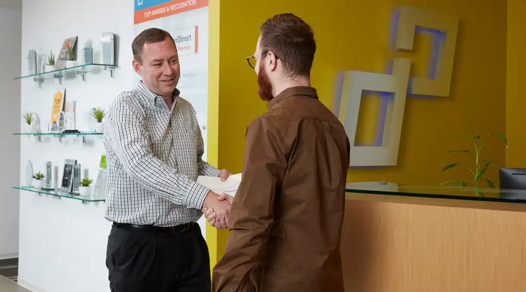 Two colleagues shaking hands in a modern office reception area.