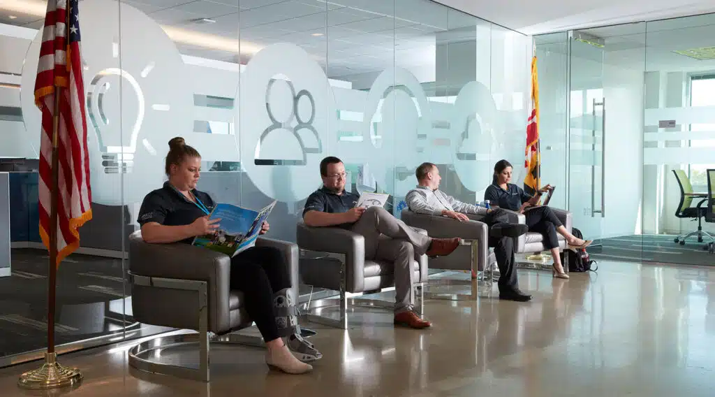 Employees seated in a modern office lobby with glass-etched icons and an American flag.