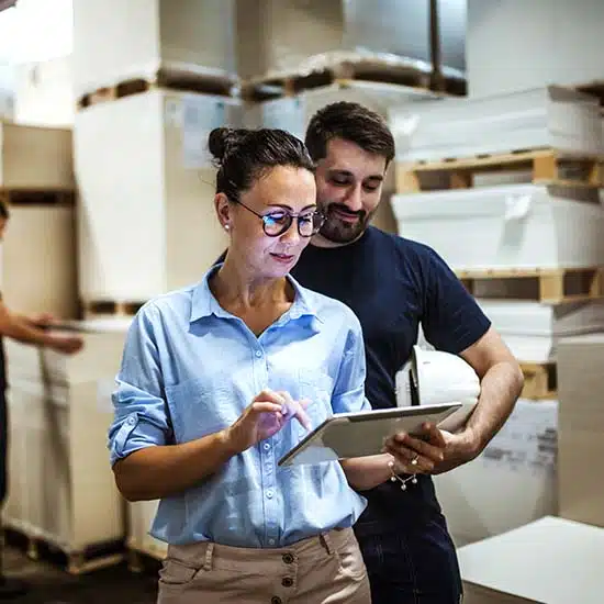 Two logistics workers reviewing data on a digital tablet in a warehouse setting
