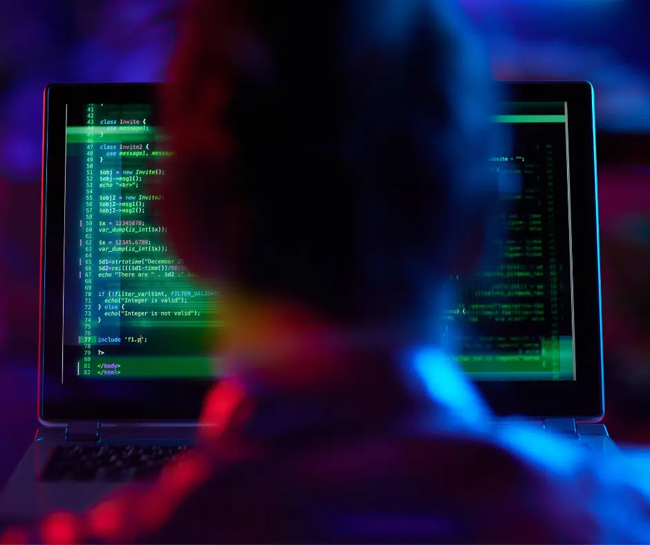 Hacker sitting in front of a laptop displaying code used for a data breach